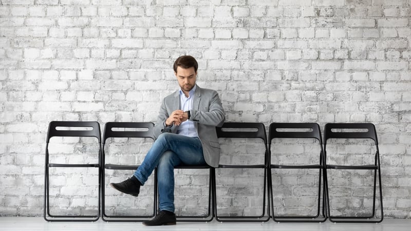 Man sitzt auf die Uhr schauend auf einem Stuhl vor einem Raum