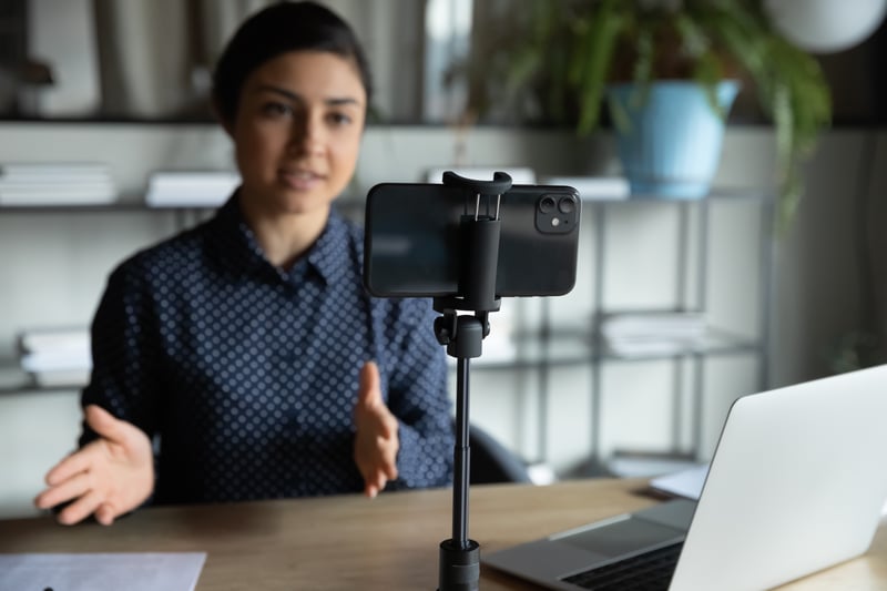 Frau am Schreibtisch vor aufgestelltem Handy für VideoChat