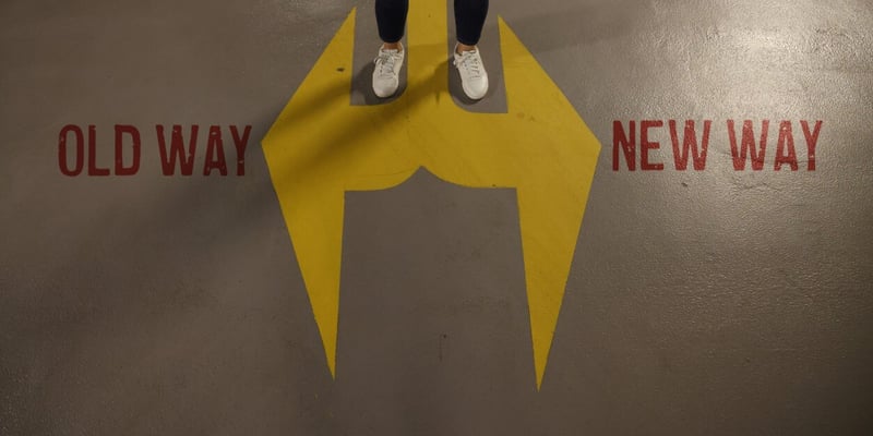 Bild von Füßen, die auf einem auf den Boden aufgemalten Pfeil stehen, der in zwei Richtungen zeigt, mit Beschriftung "old way" und "new way"