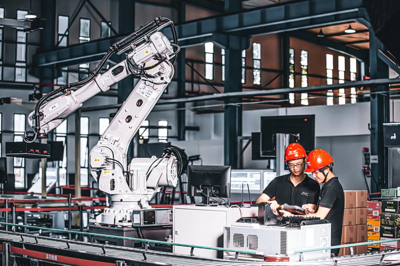 2 Arbeiter mit Helm neben Roboterarmn