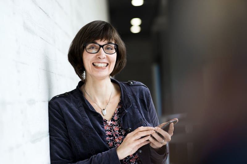 Frau mit Smartphone lehnt an Wand