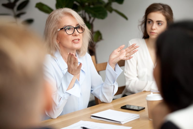 Mittelalte Frau mit Brille erklärt etwas dem Team