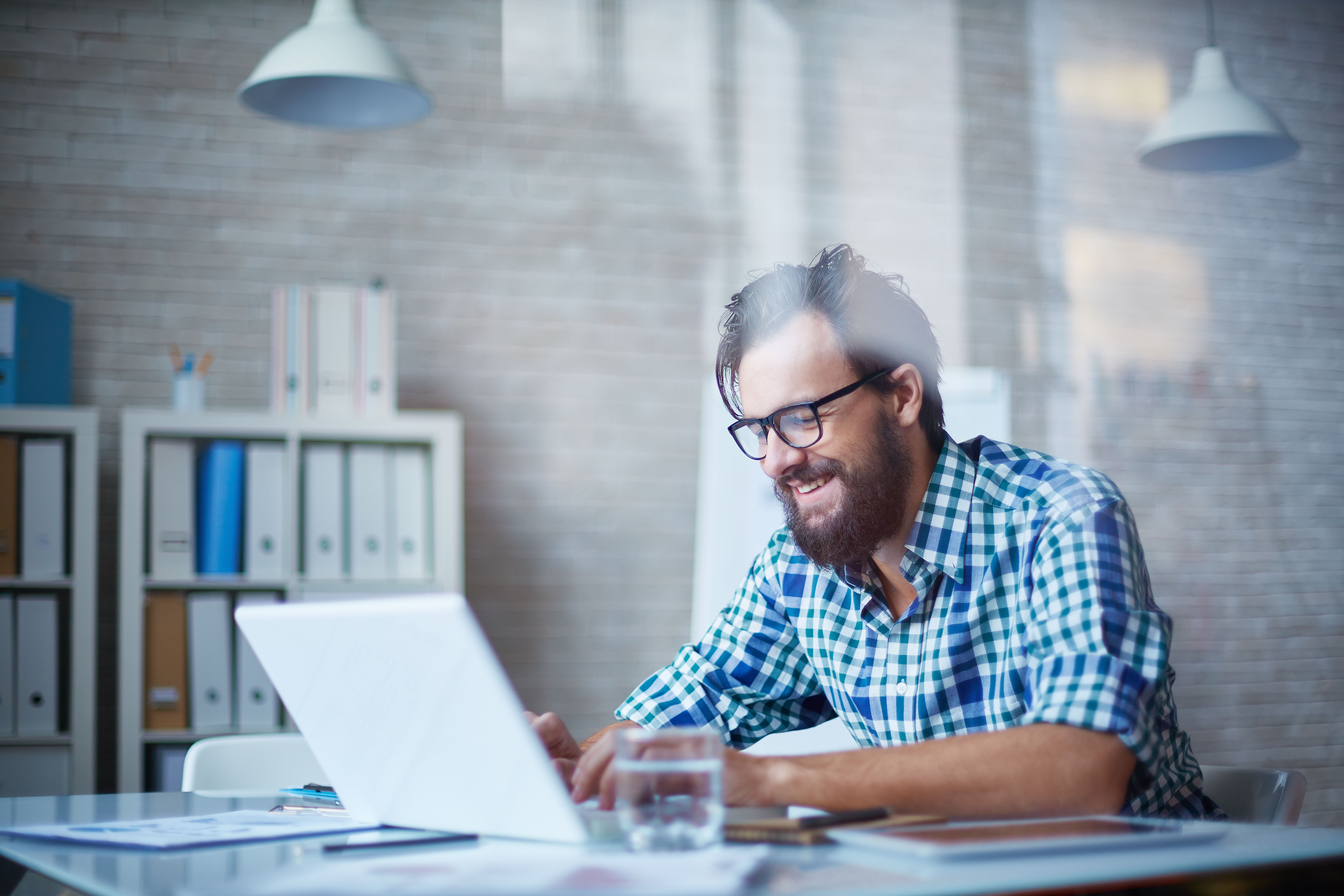 Mann mit Bart und Brille an Schreibtisch arbeitet an Laptop