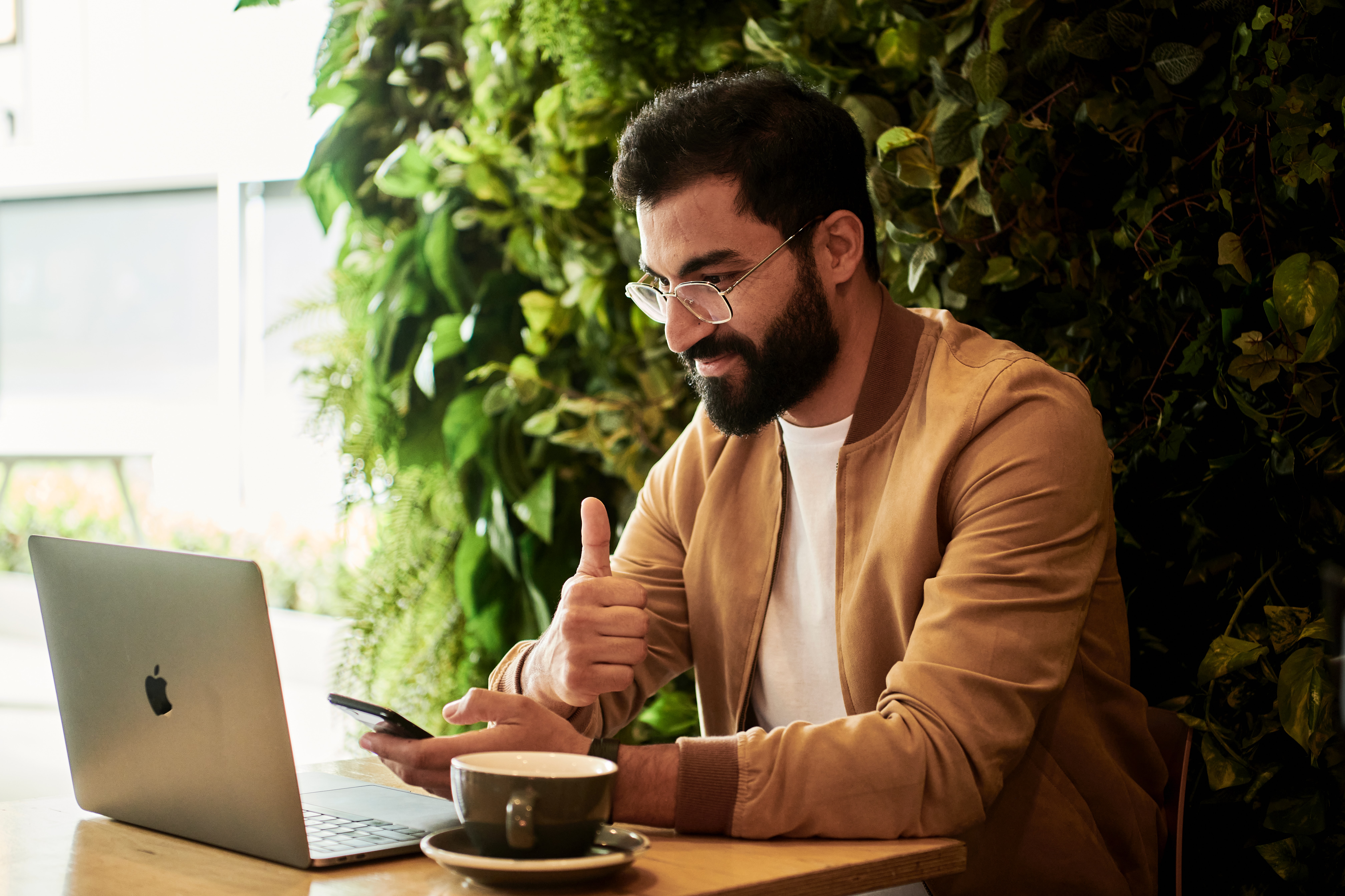 Mann mit Brille sitzt vor Laptop und Smartphone